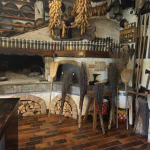Čarovniške metle iz šibja stojijo pred krušno pečjo in ognjiščem v kuhinji Kluba gurmanov Skaručna, pripravljeni za kulinarično delavnico in team building za noč čarovnic